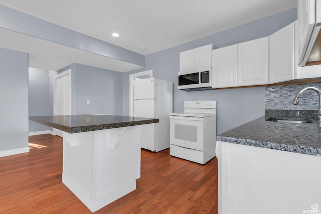 kitchen with white appliances, dark wood-style flooring, backsplash, a sink, and white cabinets