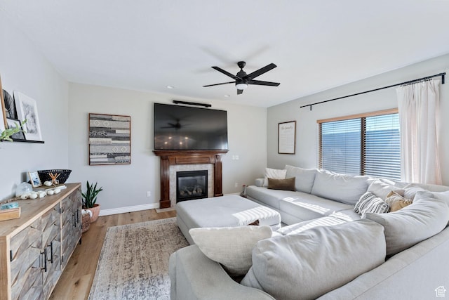 living room featuring light wood-style flooring, baseboards, a fireplace, and ceiling fan