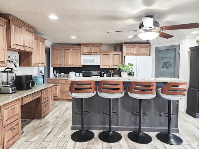 kitchen with white appliances, light wood-type flooring, ceiling fan, and a breakfast bar