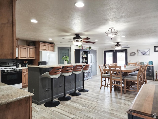 kitchen with white appliances, a breakfast bar area, light countertops, and a ceiling fan