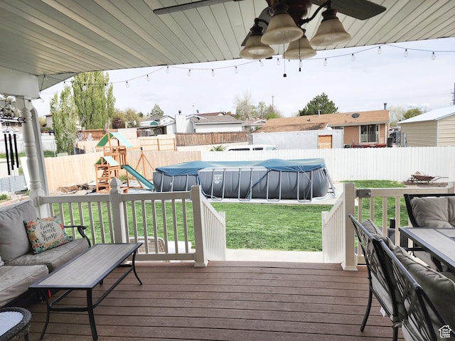 deck featuring a playground, a fenced in pool, a fenced backyard, a ceiling fan, and a lawn