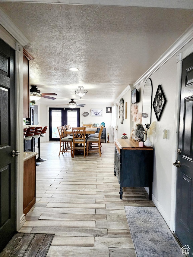 foyer featuring a textured ceiling, crown molding, baseboards, ceiling fan, and light wood-type flooring
