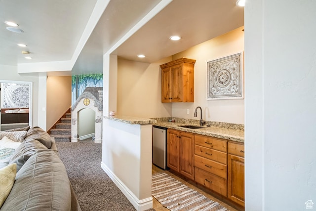 kitchen with light stone counters, a sink, dishwasher, open floor plan, and light colored carpet