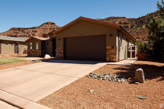 484 E Mohawk Dr, Kanab, UT 84741 - view of front of house featuring stucco siding, stone siding, driveway, a mountain view, and a garage