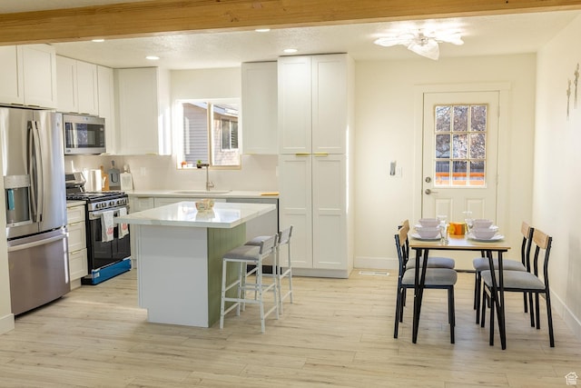kitchen with a kitchen bar, stainless steel appliances, a kitchen island, a sink, and light wood-type flooring