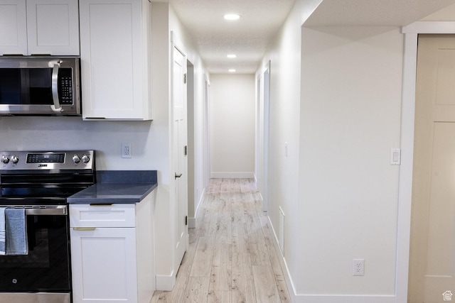 kitchen featuring recessed lighting, stainless steel appliances, baseboards, dark countertops, and light wood finished floors