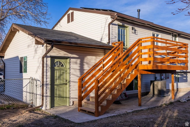 back of house with a shingled roof, fence, and stairway