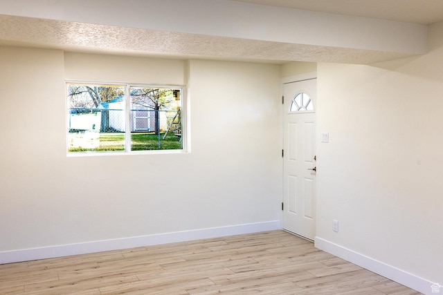 foyer entrance with baseboards, light wood-style floors, and a textured ceiling