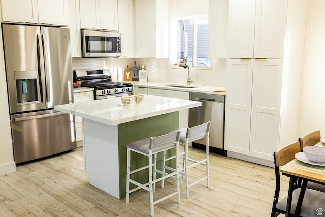 kitchen with a kitchen island, a sink, appliances with stainless steel finishes, and light wood-type flooring