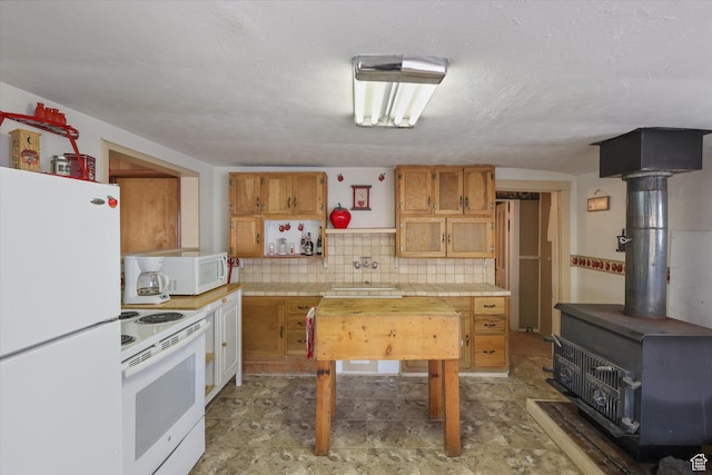 kitchen with white appliances, tasteful backsplash, a sink, a wood stove, and brown cabinetry
