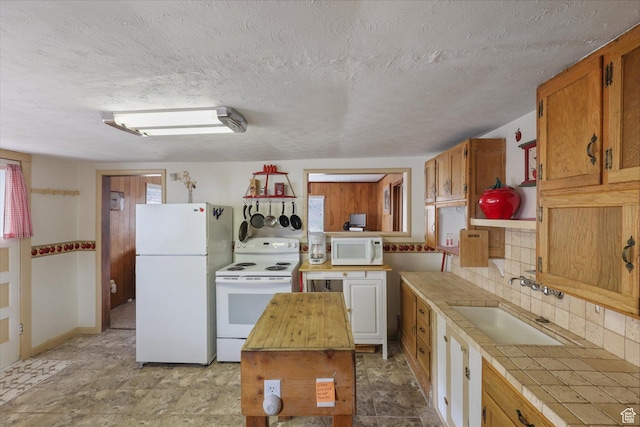 kitchen featuring a textured ceiling, tile counters, white appliances, a sink, and backsplash