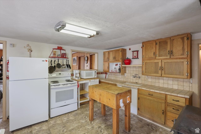 kitchen with tasteful backsplash, white appliances, a textured ceiling, a sink, and brown cabinets