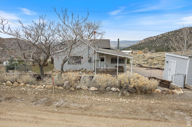 view of front of house featuring covered porch, roof with shingles, an outbuilding, a storage unit, and a mountain view