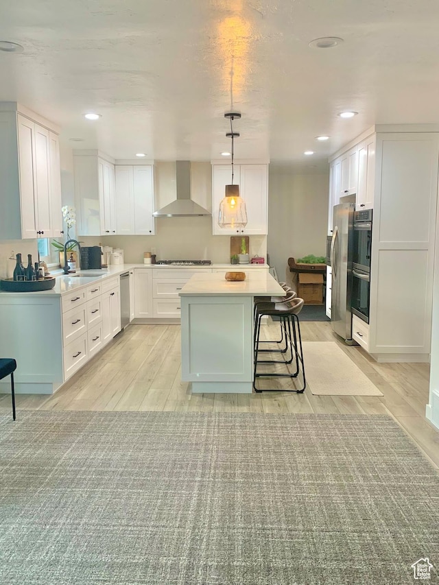 5188 S Saddleback Dr, Holladay, UT 84117 - kitchen featuring wall chimney exhaust hood, stainless steel appliances, white cabinets, light wood finished floors, and a kitchen island