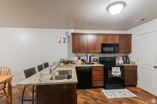 kitchen with a sink, a peninsula, dark wood-style floors, visible vents, and black appliances