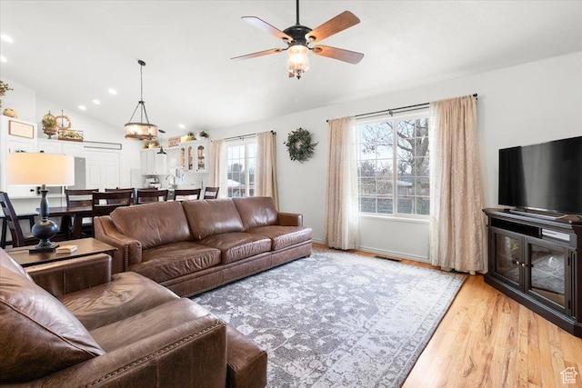 living area featuring visible vents, light wood finished floors, baseboards, lofted ceiling, and ceiling fan with notable chandelier