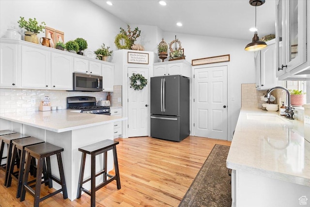 kitchen featuring a sink, a kitchen bar, a peninsula, stainless steel appliances, and white cabinets