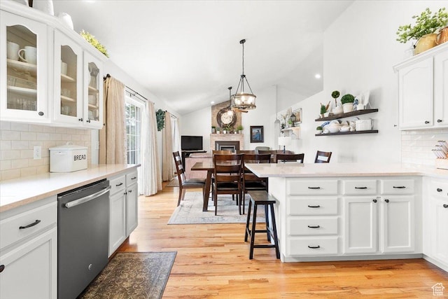 kitchen with white cabinets, dishwasher, light wood-type flooring, vaulted ceiling, and a kitchen breakfast bar