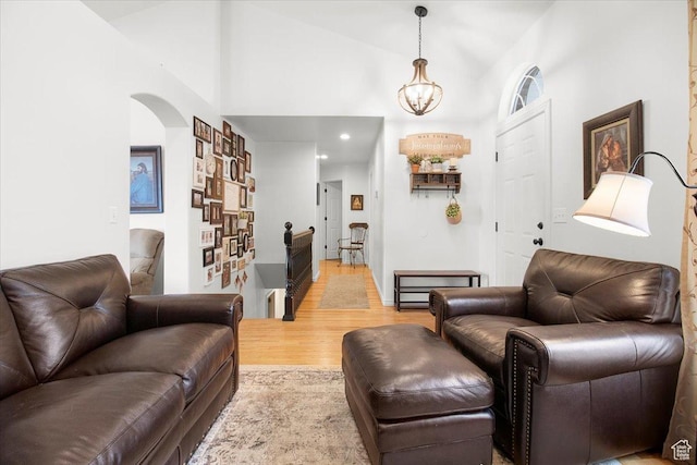 living area with high vaulted ceiling, light wood finished floors, arched walkways, recessed lighting, and an inviting chandelier
