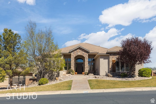 view of front facade with stucco siding, a tile roof, stone siding, and a front yard