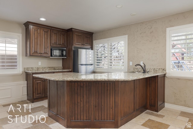 2445 E 2860 S, St George, UT 84790 - kitchen with a peninsula, light stone countertops, wallpapered walls, black microwave, and freestanding refrigerator