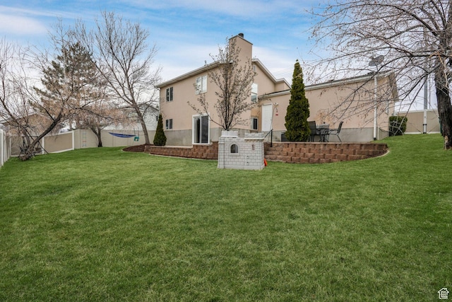 rear view of house with stucco siding, a chimney, fence, and a lawn