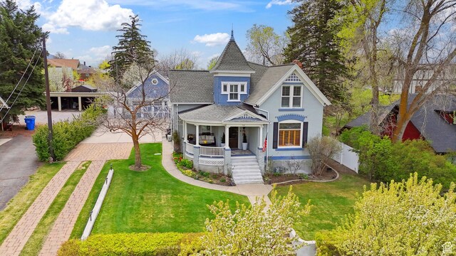 victorian home featuring covered porch, stairway, a front yard, and roof with shingles