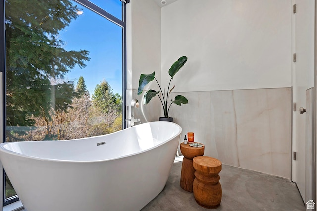 full bathroom featuring concrete floors, a freestanding tub, and wainscoting