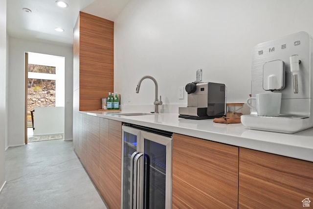 kitchen with finished concrete flooring, a sink, beverage cooler, modern cabinets, and brown cabinetry