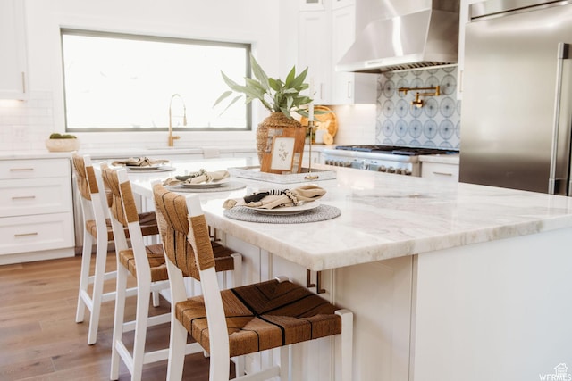 1154 Fawn, Pleasant View, UT 84414 - kitchen featuring light wood finished floors, wall chimney exhaust hood, light stone countertops, a kitchen breakfast bar, and white cabinets
