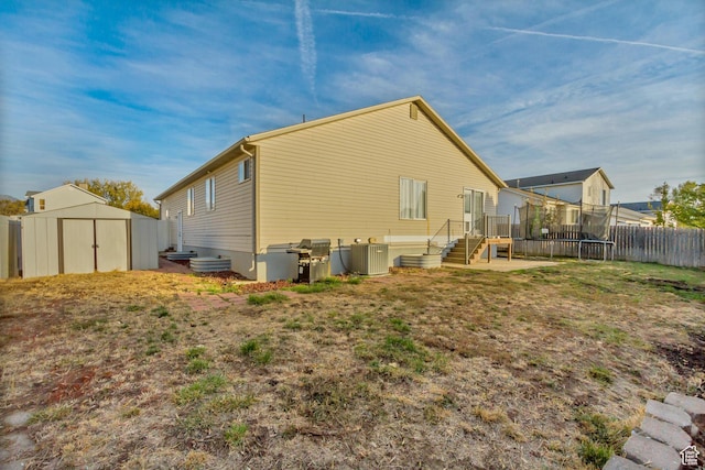 rear view of property featuring central air condition unit, fence, a storage shed, a trampoline, and an outdoor structure