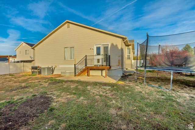 rear view of property with a trampoline, fence, central AC unit, and a yard