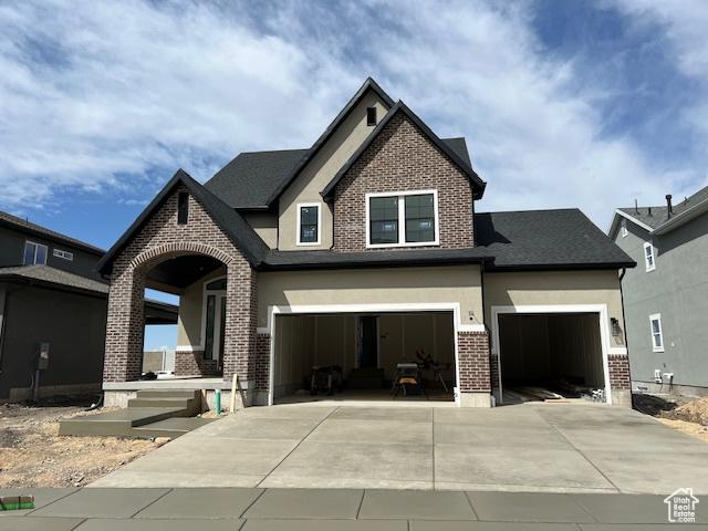 craftsman-style home with stucco siding, an attached garage, brick siding, and driveway