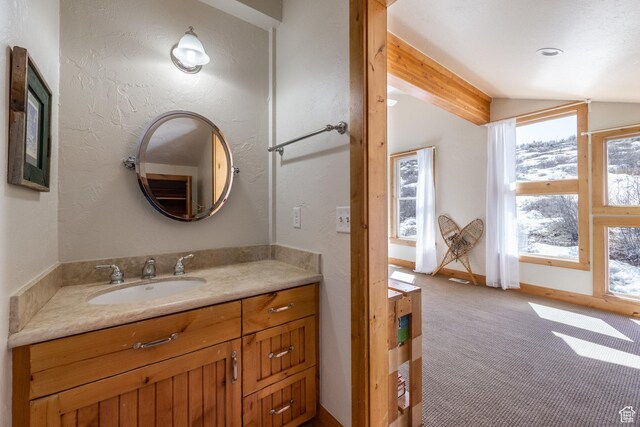 bathroom with vanity, a textured wall, and lofted ceiling