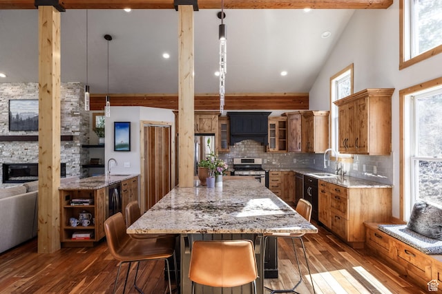 kitchen with brown cabinetry, a center island, dark wood finished floors, high vaulted ceiling, and stainless steel gas range