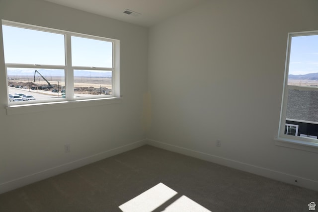unfurnished room with baseboards, visible vents, dark colored carpet, and a healthy amount of sunlight