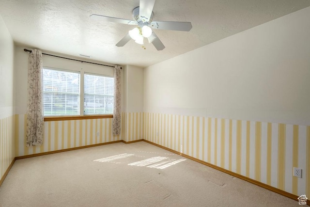 carpeted empty room with a textured ceiling, a ceiling fan, and baseboards