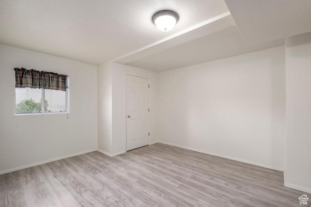spare room with light wood-style flooring, baseboards, and a textured ceiling