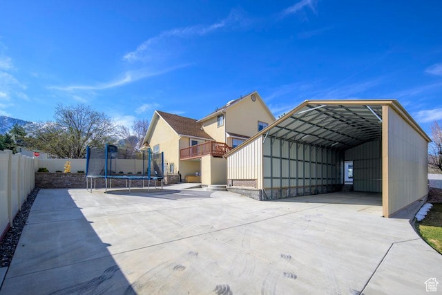 back of property with a detached carport, a trampoline, fence, and driveway