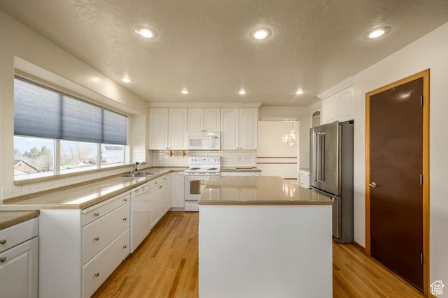 kitchen featuring white appliances, a center island, decorative backsplash, light wood-style floors, and white cabinets