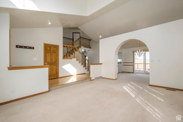 empty room featuring a chandelier, carpet, high vaulted ceiling, arched walkways, and stairway