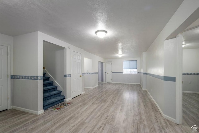 basement featuring a textured ceiling, wood finished floors, stairs, and baseboards