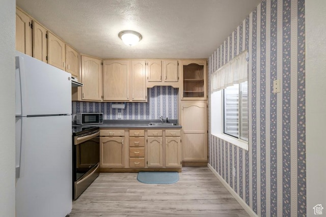 kitchen featuring appliances with stainless steel finishes, wallpapered walls, dark countertops, light wood-type flooring, and light brown cabinets