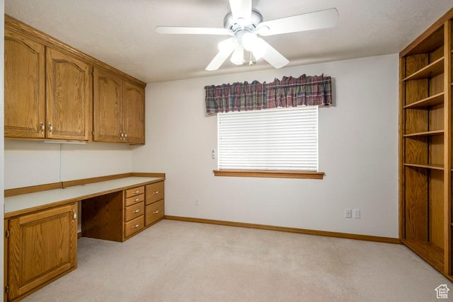 unfurnished office featuring built in desk, light colored carpet, a ceiling fan, and baseboards