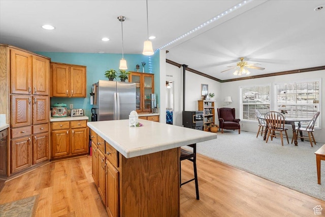 kitchen with a kitchen breakfast bar, light countertops, a kitchen island, freestanding refrigerator, and brown cabinets