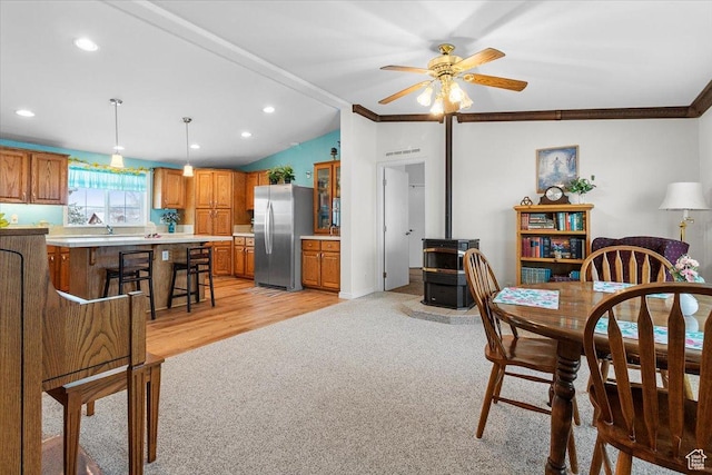 dining space featuring light colored carpet, vaulted ceiling, a wood stove, ornamental molding, and ceiling fan