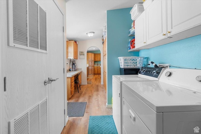 laundry room featuring visible vents, independent washer and dryer, light wood finished floors, arched walkways, and cabinet space