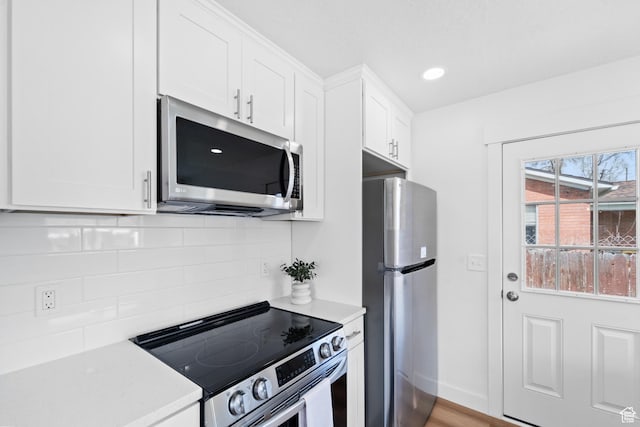kitchen with light countertops, backsplash, white cabinetry, appliances with stainless steel finishes, and baseboards