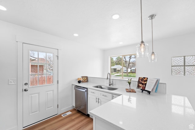 kitchen featuring light countertops, a sink, a peninsula, stainless steel dishwasher, and white cabinets