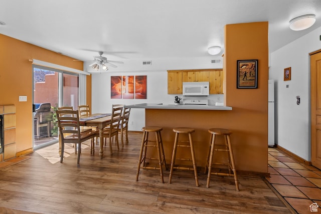 3418 E La Camino, Moab, UT 84532 - kitchen featuring wood finished floors, a kitchen breakfast bar, a peninsula, white appliances, and visible vents